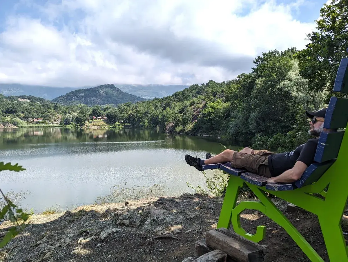 Jan liegt auf der grünen Big Bench Montalto Dora am Lago Pistono und bewundert den Blick über den See und die dahinter liegenden Berge