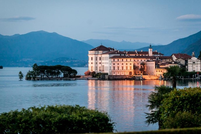 Hotel Villa e Palazzo Aminta at twilight, beautifully illuminated and reflecting on the calm waters of Lake Maggiore, a prime example of luxury accommodations in the area. The hotel’s façade glows warmly against the twilight sky, creating a romantic and inviting atmosphere for guests looking for a luxurious lakeside stay.