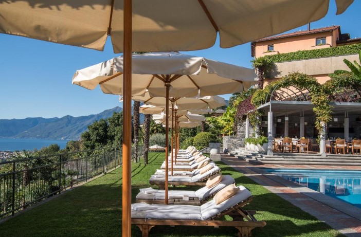 Villa Orselina’s poolside area lined with plush sunbeds and umbrellas, overlooking the scenic mountains, highlighting the exclusive ambiance of luxury hotels at Lake Maggiore. The well-manicured gardens and the strategic position on a hill offer an unrivaled view of the lake below, blending upscale comfort with breathtaking natural beauty.