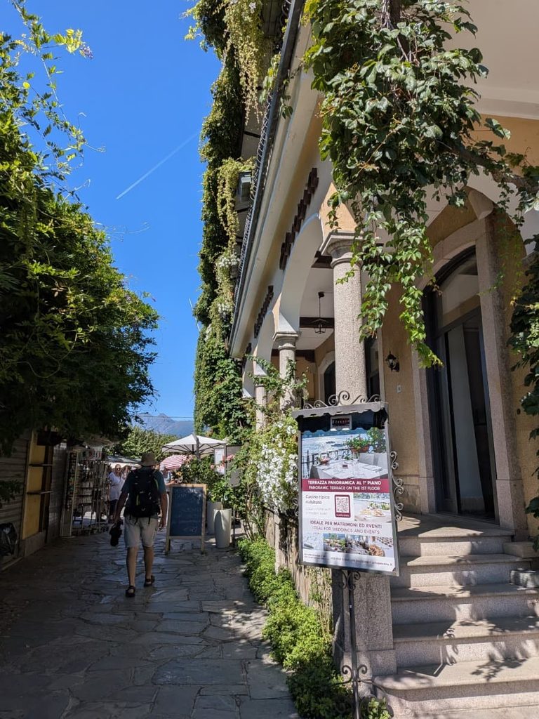 A narrow pedestrian lane on Isola Bella winds past ivy-covered buildings, cafés and small shops, capturing the relaxed village atmosphere of the Borromean Island.