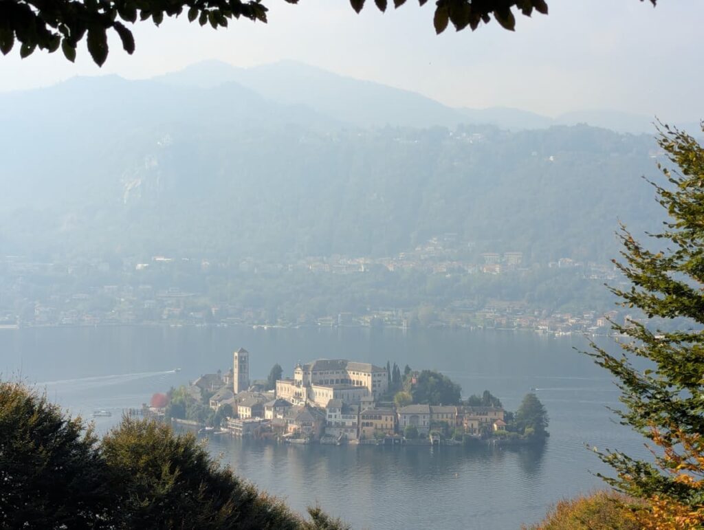 San Giulio Island sits in the calm waters of Lake Orta in Piedmont, Italy, surrounded by wooded hills and hazy mountains, a scenic stop when planning how many days to spend in Piedmont Italy.