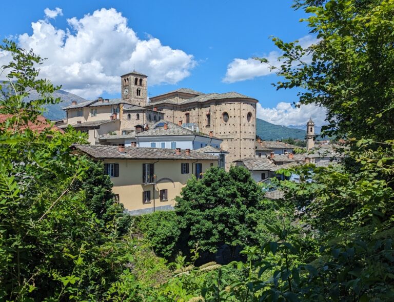 Historic stone houses and a large church rise above the green hillside in the mountain town of Prato Sesia, a charming cultural stop to include when planning how many days to spend in Piedmont Italy.